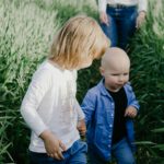 girl in white long sleeve shirt and blue pants sitting on green grass field during daytime