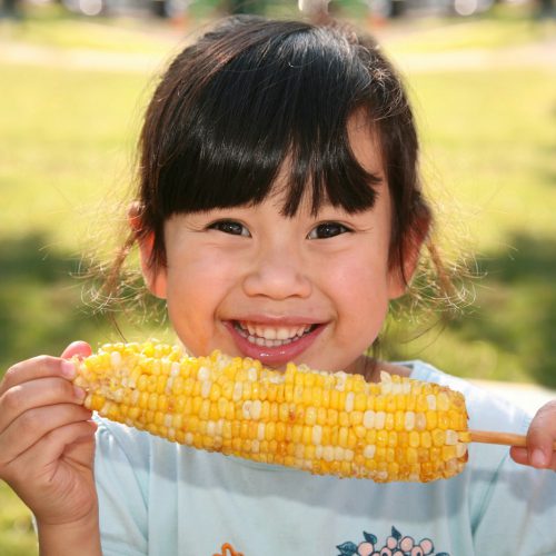smiling girl holding cooked corn during daytime